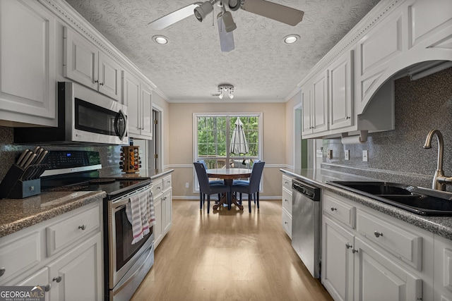 kitchen featuring appliances with stainless steel finishes, a sink, ornamental molding, white cabinets, and backsplash