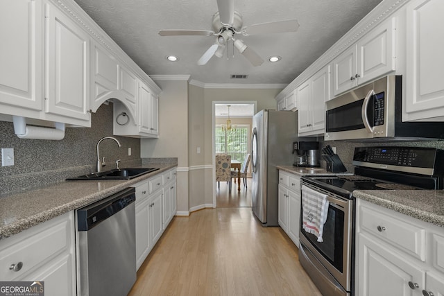 kitchen featuring appliances with stainless steel finishes, a sink, white cabinetry, a ceiling fan, and crown molding