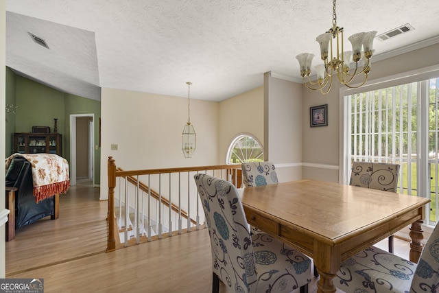 dining room featuring light wood-type flooring, healthy amount of natural light, a chandelier, a textured ceiling, and ornamental molding