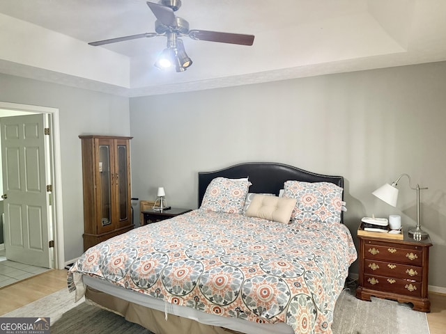 bedroom with wood finished floors, baseboards, a ceiling fan, and a raised ceiling