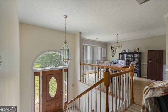 entryway featuring a chandelier, light wood-style flooring, a textured ceiling, and baseboards