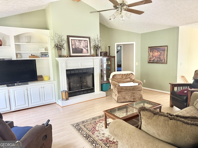 living area featuring lofted ceiling, light wood-type flooring, ceiling fan, a fireplace with raised hearth, and built in features