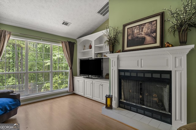 living room featuring a fireplace with raised hearth, vaulted ceiling, light wood-style flooring, and a textured ceiling