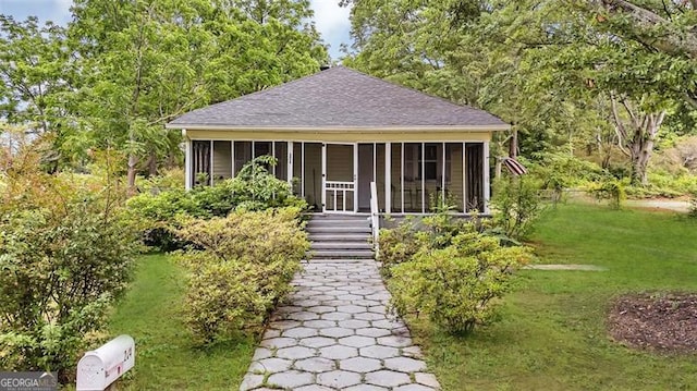 view of front facade with a sunroom, roof with shingles, and a front lawn