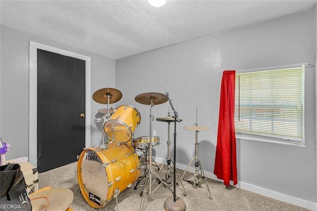 recreation room with carpet floors, a textured ceiling, baseboards, and a textured wall