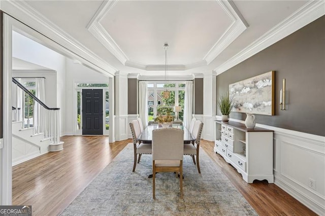 dining area with a decorative wall, wood finished floors, crown molding, a tray ceiling, and stairway