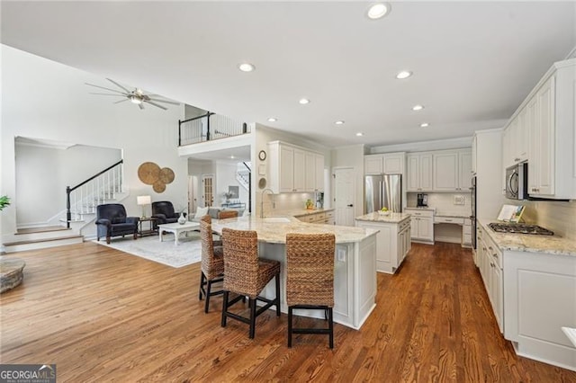 kitchen featuring appliances with stainless steel finishes, open floor plan, a peninsula, light stone counters, and recessed lighting