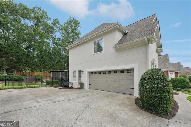 view of property exterior featuring stucco siding, driveway, fence, roof with shingles, and an attached garage