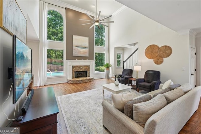 living room featuring a stone fireplace, stairway, a high ceiling, a ceiling fan, and ornamental molding