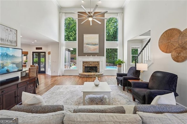 living room with a towering ceiling, ceiling fan, wood finished floors, stairs, and ornamental molding