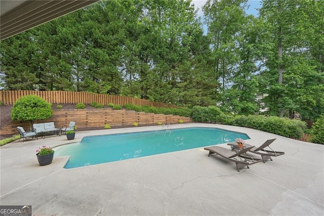 view of swimming pool with a patio area, a fenced backyard, and view of wooded area