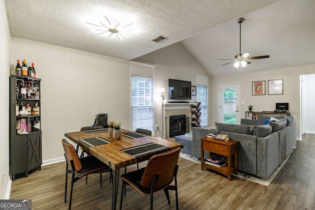 dining area with wood finished floors, a fireplace, a textured ceiling, ceiling fan, and lofted ceiling