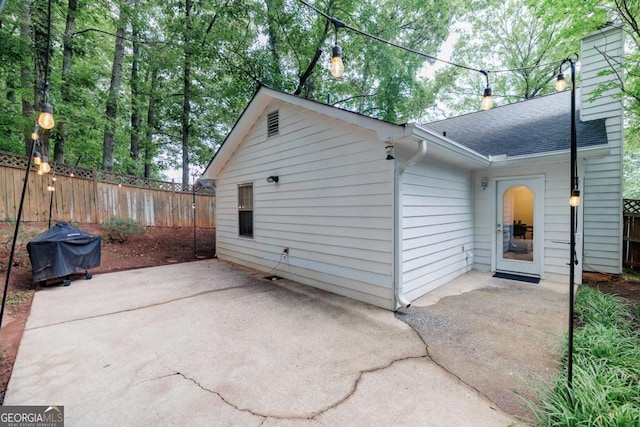 view of side of home with a patio, fence, a shingled roof, and a chimney