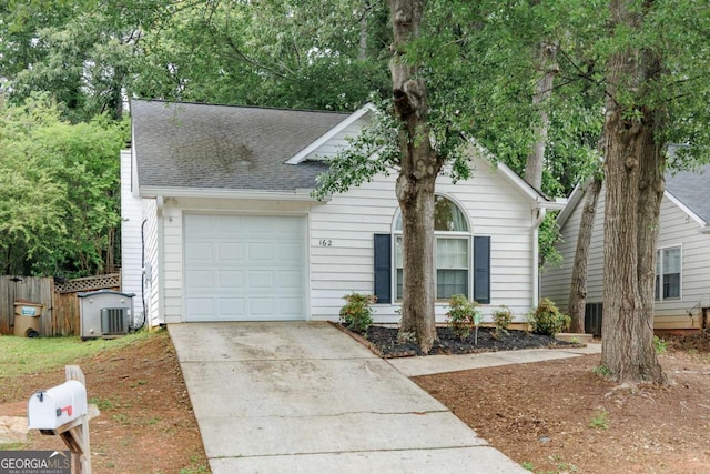 view of property hidden behind natural elements featuring a garage, driveway, roof with shingles, and central AC unit