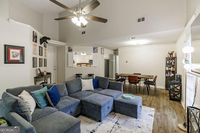 living room with high vaulted ceiling, a ceiling fan, light wood-type flooring, and baseboards
