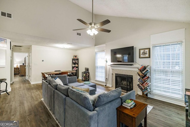 living area featuring lofted ceiling, ceiling fan, a tile fireplace, wood finished floors, and baseboards