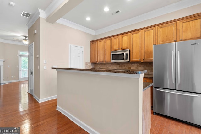 kitchen featuring stainless steel appliances, crown molding, backsplash, brown cabinetry, and wood finished floors