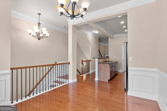 corridor featuring a chandelier, an upstairs landing, a sink, wood finished floors, and crown molding