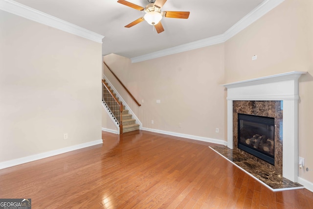 unfurnished living room featuring ornamental molding, a ceiling fan, stairs, a premium fireplace, and wood finished floors