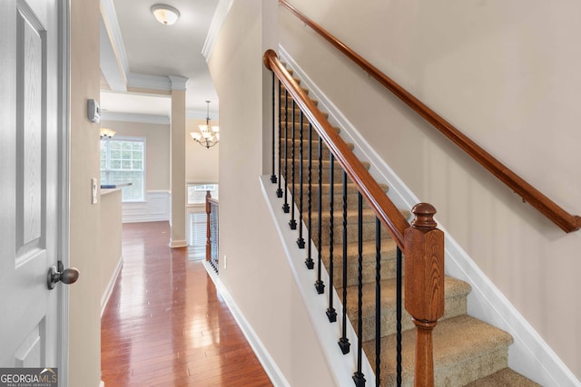 staircase with a chandelier, ornamental molding, wood finished floors, and baseboards