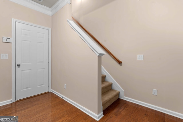 staircase with wood finished floors, baseboards, and crown molding
