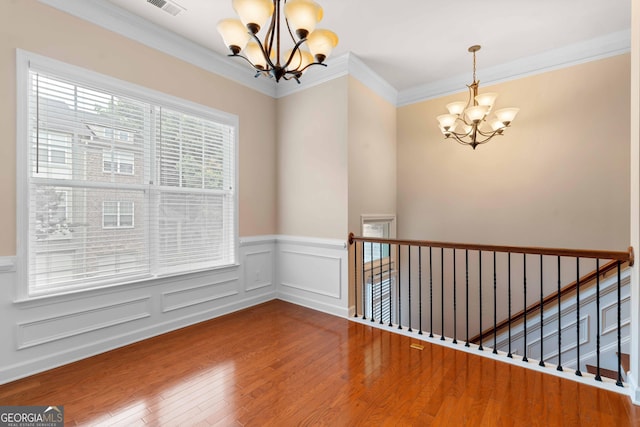 unfurnished room with a chandelier, wood finished floors, a wainscoted wall, ornamental molding, and a decorative wall