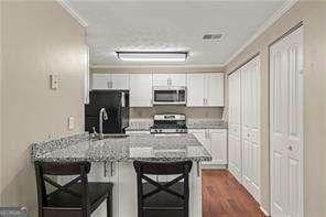 1371 Keys Lake Dr NE, Atlanta, GA 30319 - kitchen featuring stainless steel appliances, ornamental molding, a peninsula, white cabinetry, and a breakfast bar