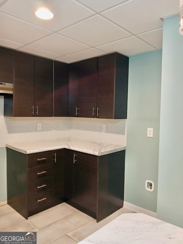 1202 Laurel Cliff Dr SE, Smyrna, GA 30082 - kitchen with backsplash, under cabinet range hood, a drop ceiling, dark brown cabinetry, and light tile patterned flooring