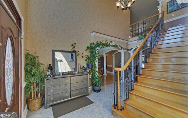 foyer entrance with a towering ceiling, ornate columns, a chandelier, stairs, and granite tiled floors
