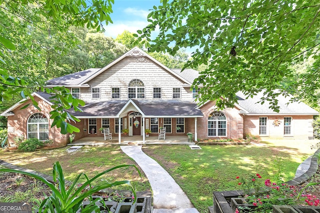 back of property with a yard, covered porch, brick siding, and a shingled roof