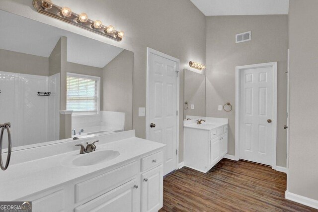 1280 Chandler Ridge Dr, Lawrenceville, GA 30045 - bathroom featuring two vanities, vaulted ceiling, a bath, wood finished floors, and a shower