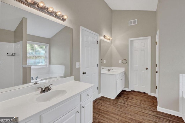 1280 Chandler Ridge Dr, Lawrenceville, GA 30045 - bathroom featuring vaulted ceiling, two vanities, a garden tub, wood finished floors, and walk in shower