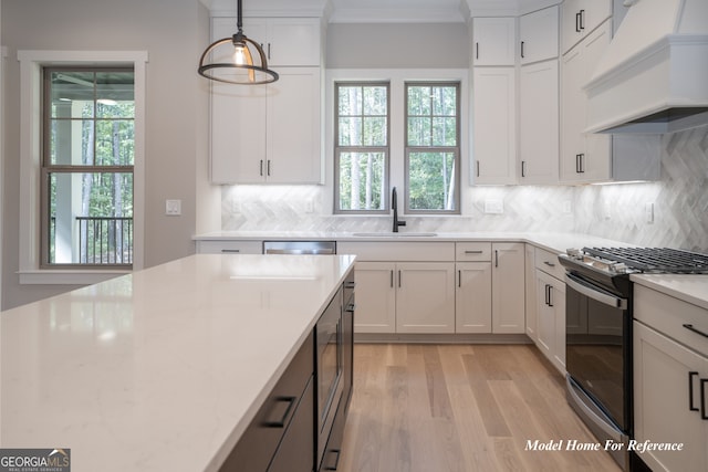 kitchen with gas range, a sink, premium range hood, light wood-type flooring, and tasteful backsplash
