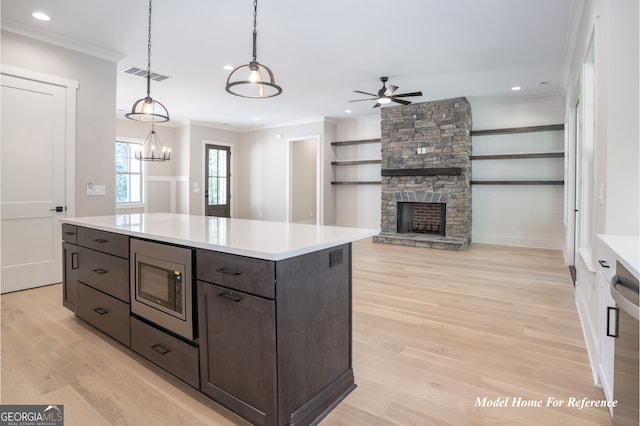 kitchen featuring stainless steel microwave, light wood finished floors, ornamental molding, a fireplace, and dark brown cabinetry