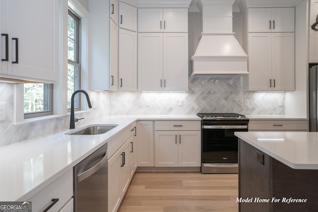 kitchen featuring appliances with stainless steel finishes, a sink, custom range hood, light countertops, and backsplash