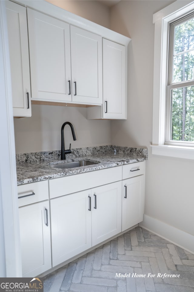kitchen with a sink, white cabinets, light stone countertops, baseboards, and brick patterned flooring