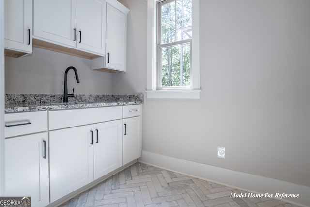 kitchen with baseboards, white cabinets, brick patterned flooring, light stone counters, and a sink