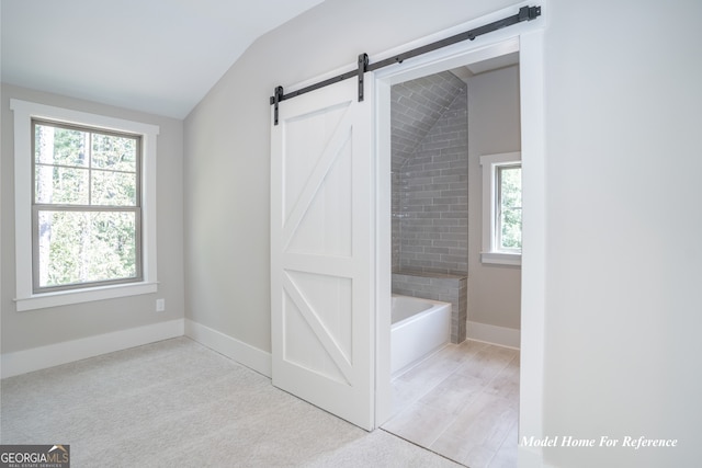 bathroom featuring lofted ceiling, plenty of natural light, a tub to relax in, and baseboards