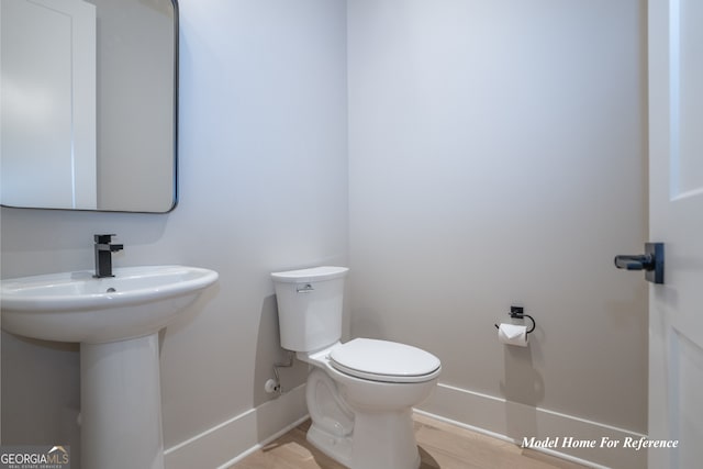 half bath with baseboards, toilet, wood finished floors, and a sink