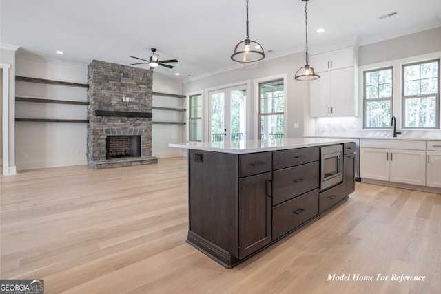 kitchen featuring stainless steel microwave, ceiling fan, white cabinetry, light countertops, and crown molding