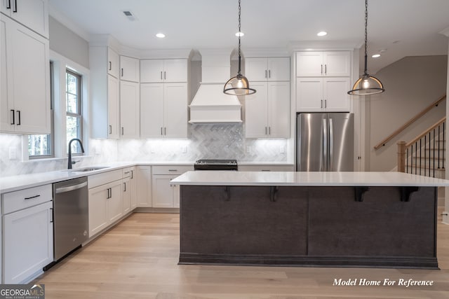 kitchen with appliances with stainless steel finishes, a sink, custom exhaust hood, light wood-style flooring, and white cabinets