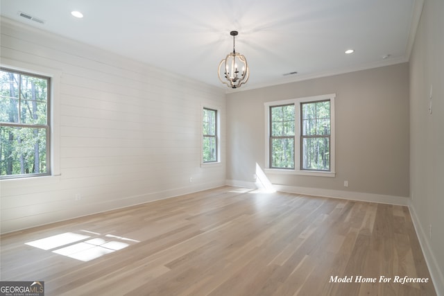 empty room featuring a chandelier, light wood-type flooring, baseboards, ornamental molding, and recessed lighting