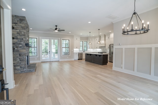 unfurnished living room featuring ornamental molding, a chandelier, ceiling fan, healthy amount of natural light, and light wood-style floors