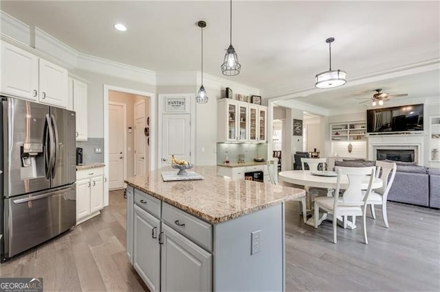 kitchen featuring stainless steel fridge, crown molding, white cabinets, ceiling fan, and a fireplace
