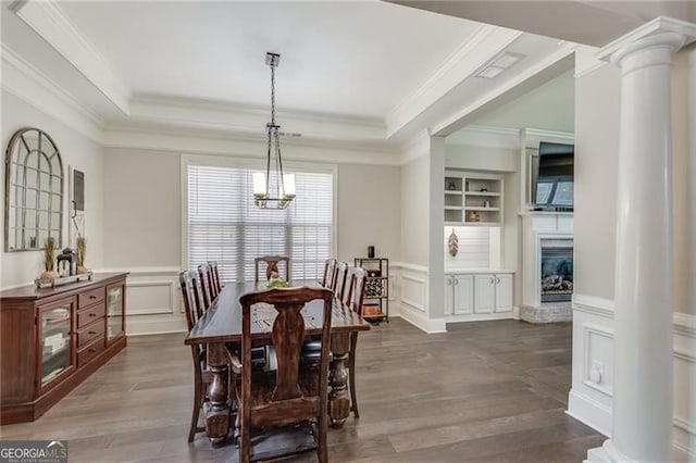 dining area with decorative columns, a decorative wall, wood finished floors, built in shelves, and a chandelier