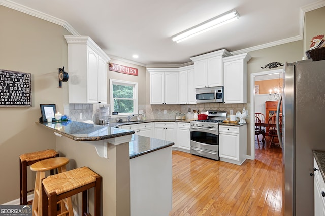 138 Knightwood Pt, Acworth, GA 30101 - kitchen featuring appliances with stainless steel finishes, a peninsula, ornamental molding, a breakfast bar area, and dark stone counters