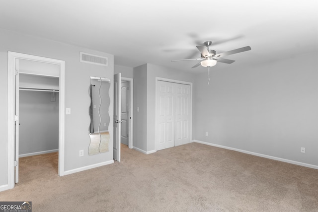 unfurnished bedroom with carpet, baseboards, a spacious closet, and a ceiling fan