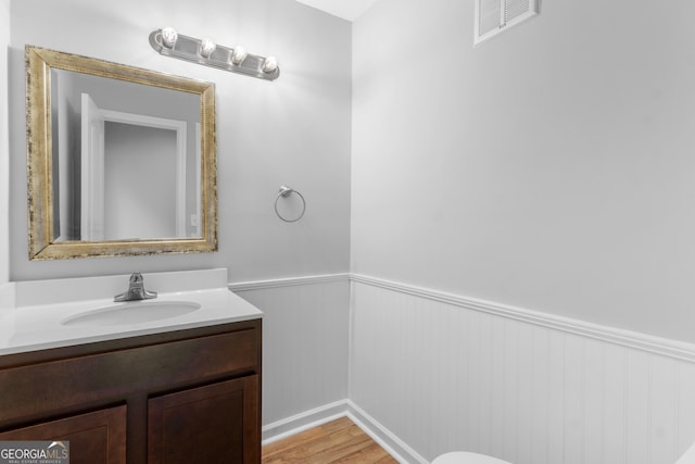 bathroom with a wainscoted wall, vanity, and wood finished floors