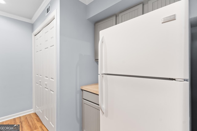 kitchen featuring freestanding refrigerator, ornamental molding, light wood finished floors, light countertops, and baseboards