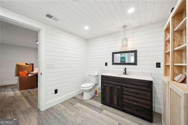 bathroom with wooden ceiling, toilet, wood finished floors, vanity, and wood walls
